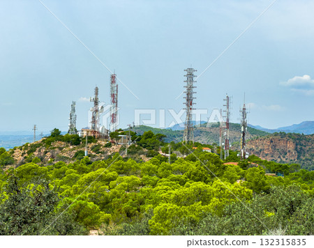 Communication towers rise above lush greenery in a scenic landscape under a bright sky near the hills during a clear afternoon Communication towers rise above lush greenery in a scenic landscape under a bright sky near the hills during a clear afternoon 132315835
