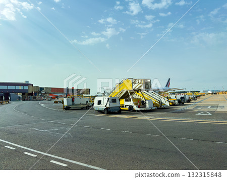 Busy airport terminal with bright yellow ground support vehicles preparing for the day ahead under a clear sky Busy airport terminal with bright yellow ground support vehicles preparing for the day ahead under a clear sky 132315848