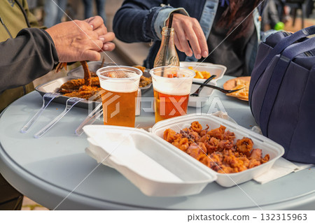 Close-up of hands people sharing fried seafood, fries, beer at outdoor table during casual street meal. Concept of street food, friendship, relaxed social dining, takeaway packaging and drinks Close-up of hands people sharing fried seafood, fries, beer at outdoor table during casual street meal. Concept of street food, friendship, relaxed social dining, takeaway packaging and drinks 132315963