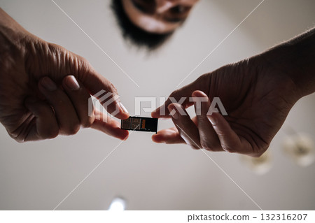 Low-angle view of man replacing sim card in mobile phone, providing efficient and reliable technical support to customer. Concept of smartphone maintenance and service. Low-angle view of man replacing sim card in mobile phone, providing efficient and reliable technical support to customer. Concept of smartphone maintenance and service. 132316207