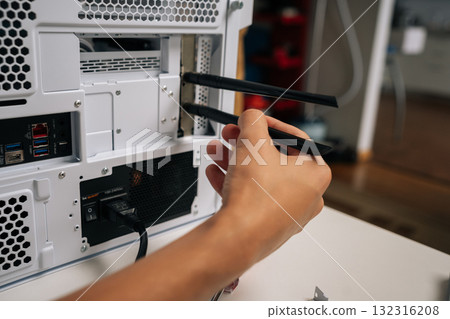Technician male installing wifi module with two antennas into desktop computer case, enhancing connectivity and network performance, during upgrading or assembling PC at workshop 132316208