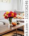 Autumn, fall cozy mood composition for hygge home decor. Bouquet of fresh multicolor dahlia flowers, small pumpkin, burning candles on the coffee table in modern living room. Selective focus. Vertical 132316246