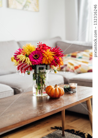 Autumn, fall cozy mood composition for hygge home decor. Bouquet of fresh multicolor dahlia flowers, small pumpkin, burning candles on the coffee table in modern living room. Selective focus. Vertical Autumn, fall cozy mood composition for hygge home decor. Bouquet of fresh multicolor dahlia flowers, small pumpkin, burning candles on the coffee table in modern living room. Selective focus. Vertical 132316246