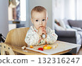 Cute baby learning to eat food with baby spoon by himself on high chair baby led weaning or blw. Infant self-feeding solid food, making mess, fine motor development. Kid enjoying healthy nutrition. 132316247