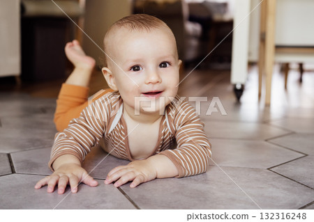 Happy, laughing baby lying on tiled floor at home for child development, wellness and growth. Cheerful active little infant kid training physical skills, smiling, learning to crawl, playing and relax. Happy, laughing baby lying on tiled floor at home for child development, wellness and growth. Cheerful active little infant kid training physical skills, smiling, learning to crawl, playing and relax. 132316248