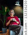 Middle aged woman relaxing with cup of hot drink in hygge stylish interior home. Lady dreaming, enjoy calm mood without stress, well being alone. Take a break and relax. Cozy fall or winter weekend. 132316250