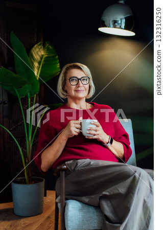 Middle aged woman relaxing with cup of hot drink in hygge stylish interior home. Lady dreaming, enjoy calm mood without stress, well being alone. Take a break and relax. Cozy fall or winter weekend. Middle aged woman relaxing with cup of hot drink in hygge stylish interior home. Lady dreaming, enjoy calm mood without stress, well being alone. Take a break and relax. Cozy fall or winter weekend. 132316250