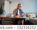 Middle aged woman reviewing expenses, managing personal finances on smartphone mobile app while sitting on couch with coffee in cozy living space. finance planning, financial balance check, budgeting 132316252