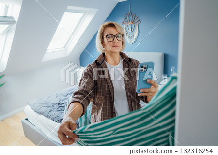 Middle aged Woman taking photo of shirt using smartphone for selling or donating her clothes. Decluttering , Sorting Clothes, And Cleaning Up wardrobe. Reuse, second-hand concept. Conscious consumer. Middle aged Woman taking photo of shirt using smartphone for selling or donating her clothes. Decluttering , Sorting Clothes, And Cleaning Up wardrobe. Reuse, second-hand concept. Conscious consumer. 132316254