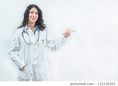 Smiling female doctor pointing at an advertisement to the side isolated. Young female doctor recommending an advertisement Smiling female doctor pointing at an advertisement to the side isolated. Young female doctor recommending an advertisement 132316263