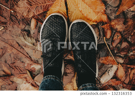 Autumnal walk through fallen leaves. A person's feet in black sneakers are seen walking on a bed of fallen autumn leaves, a cozy seasonal atmosphere Autumnal walk through fallen leaves. A person's feet in black sneakers are seen walking on a bed of fallen autumn leaves, a cozy seasonal atmosphere 132316353