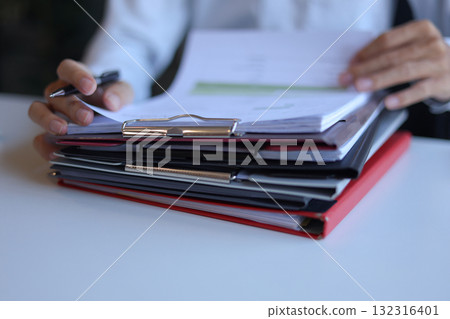Businessman working in office reading, signing stack of documents. Businessman working in office reading, signing stack of documents. 132316401