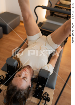 Pilates core focus, reformer movement with calm lighting, woman performs controlled leg circles Pilates core focus, reformer movement with calm lighting, woman performs controlled leg circles 132316448