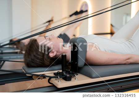 Woman lying on reformer performs controlled leg circles emphasizing core engagement and therapeutic. Woman lying on reformer performs controlled leg circles emphasizing core engagement and therapeutic. 132316455