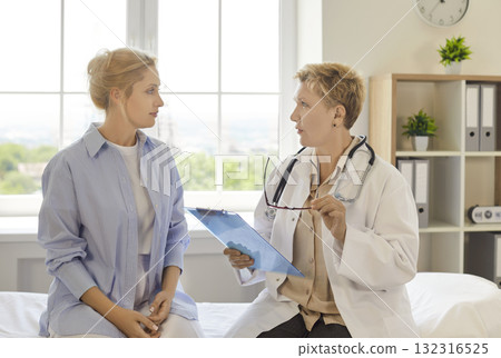 Doctor consulting young patient in clinic consultation room, holding clipboard Doctor consulting young patient in clinic consultation room, holding clipboard 132316525