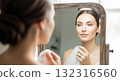 A stunning bride-to-be, with dark, wavy hair and a white slip dress, looks at her glowing reflection in an ornate golden mirror 132316560