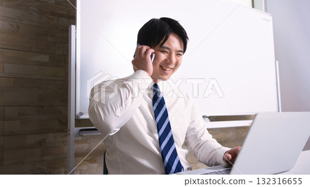 A young businessman talking on a smartphone while looking at a computer in the office 132316655