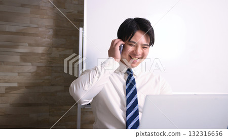 A young businessman talking on a smartphone while looking at a computer in the office 132316656