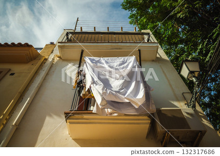 Laundry drying in the sunlight on a small balcony in the Santa Cruz district of Alicante, Spain, surrounded by warm Mediterranean architecture and blue sky. 132317686