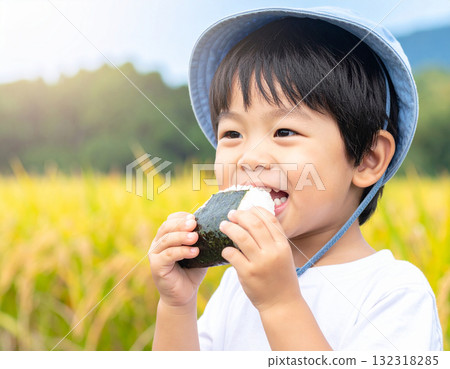 稻田裡,一個微笑的男孩正在吃著飯糰。圖片展現了新稻米、自然和食品教育。 稻田裡,一個微笑的男孩正在吃著飯糰。圖片展現了新稻米、自然和食品教育。 132318285