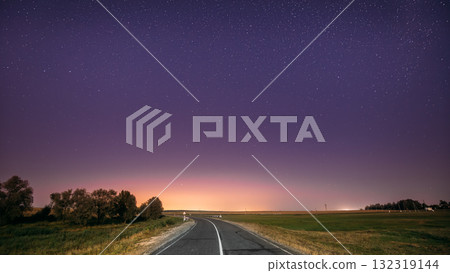 Night Starry Sky Above Country Road In Countryside And Green Field. Yellow City Lights On Background. Night View Of Natural Glowing Stars Night Starry Sky Above Country Road In Countryside And Green Field. Yellow City Lights On Background. Night View Of Natural Glowing Stars 132319144