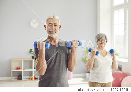 Active Senior Couple Exercising With Dumbbells In Gym Active Senior Couple Exercising With Dumbbells In Gym 132321336