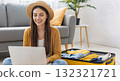 Young woman planning vacation using laptop with packed suitcase nearby 132321721
