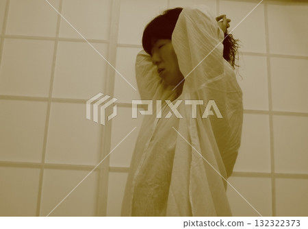 A woman wearing a white long shirt and playing with her hair after a bath A woman wearing a white long shirt and playing with her hair after a bath 132322373