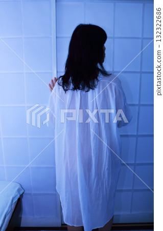 Back view of a woman wearing a long shirt standing in front of a shoji screen 132322686