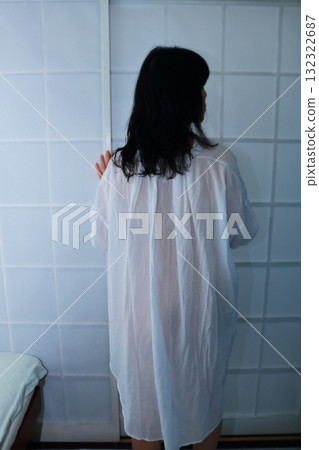 Back view of a woman wearing a long shirt standing in front of a shoji screen 132322687
