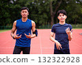 Two Asian men in sportswear standing on a running track, posing confidently before a workout session. Healthy lifestyle, teamwork, motivation, and outdoor fitness training for active individuals 132322928