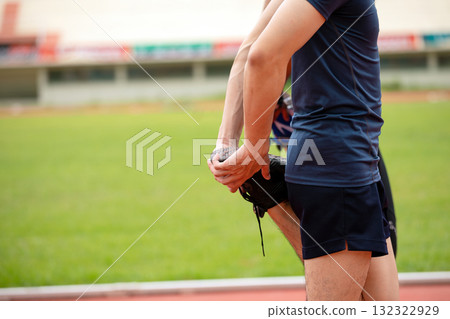 Close-up of an Asian man stretching his leg before a workout on an outdoor running track. Fitness preparation, warm-up routine, and healthy lifestyle for athletes or active individuals Close-up of an Asian man stretching his leg before a workout on an outdoor running track. Fitness preparation, warm-up routine, and healthy lifestyle for athletes or active individuals 132322929