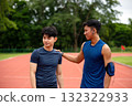 Asian male athlete putting a hand on teammate's shoulder on an outdoor track, symbolizing support, encouragement, friendship, and motivation during sports training or after competition 132322933