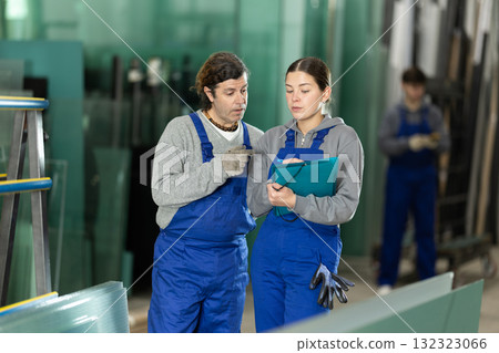 Girl and adult man glazier employees with documents speaking and advising in workshop Girl and adult man glazier employees with documents speaking and advising in workshop 132323066