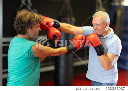 Older trainee practicing punches in sparring at boxing gym 132323087