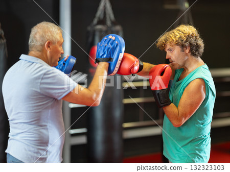 Man punches boxing paw held by trainer 132323103