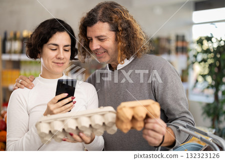 Checking expiration date of eggs - wife and husband shoppers scans QR code on label of eggs using smartphone Checking expiration date of eggs - wife and husband shoppers scans QR code on label of eggs using smartphone 132323126