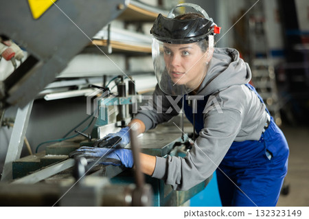 Girl employee wearing safety face shield performs hazardous work in production. 132323149