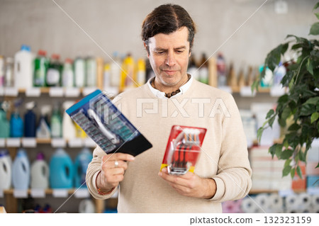 Man carefully selects razor for shaving in the household goods department of supermarket Man carefully selects razor for shaving in the household goods department of supermarket 132323159