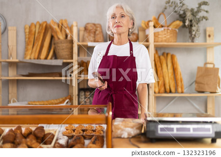 Elderly female seller with tongs in bakery Elderly female seller with tongs in bakery 132323196