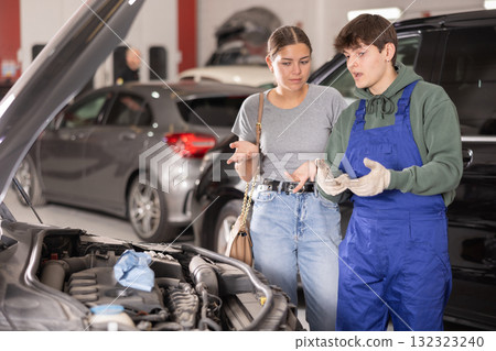 Mechanic advises woman on repairs under hood of car 132323240