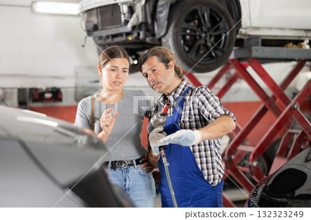 Worried woman talks about the problems of her car to an auto mechanic at car service center Worried woman talks about the problems of her car to an auto mechanic at car service center 132323249