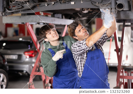 Young auto mechanic helps an experienced auto mechanic repair a car in car service center 132323260