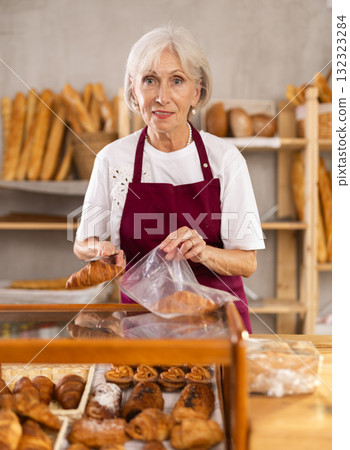 Elderly woman seller puts croissant in bag Elderly woman seller puts croissant in bag 132323284