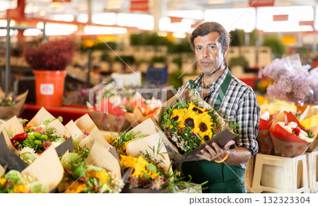 Positive male seller in apron holds designer bouquet in hands 132323304