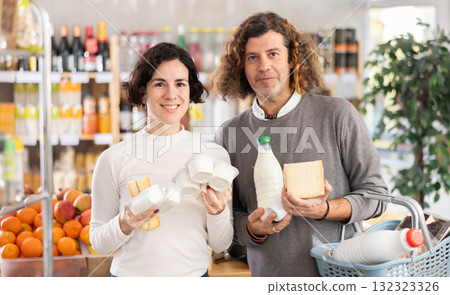 Family with various dairy products in her hands continues to make choice in grocery department of supermarket Family with various dairy products in her hands continues to make choice in grocery department of supermarket 132323326