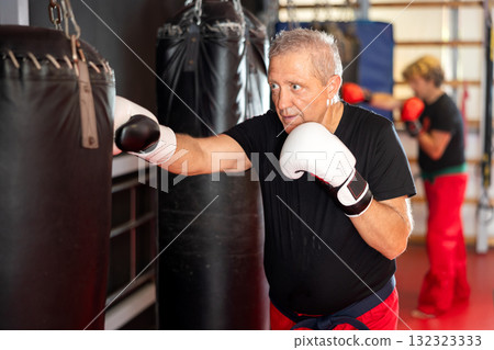 Senior karateka punching heavy bag in dojo training Senior karateka punching heavy bag in dojo training 132323333