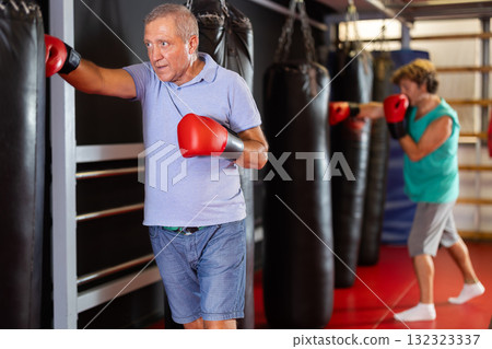 Senior man training punches on heavy bag in gym Senior man training punches on heavy bag in gym 132323337
