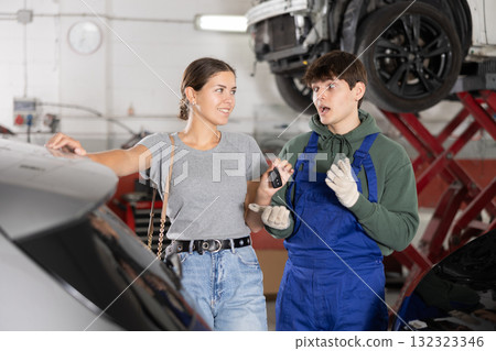 Smiling female client giving car keys to young mechanic in workshop 132323346