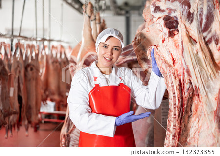 Female butcher in slaughterhouse showing piece of cow carcass 132323355